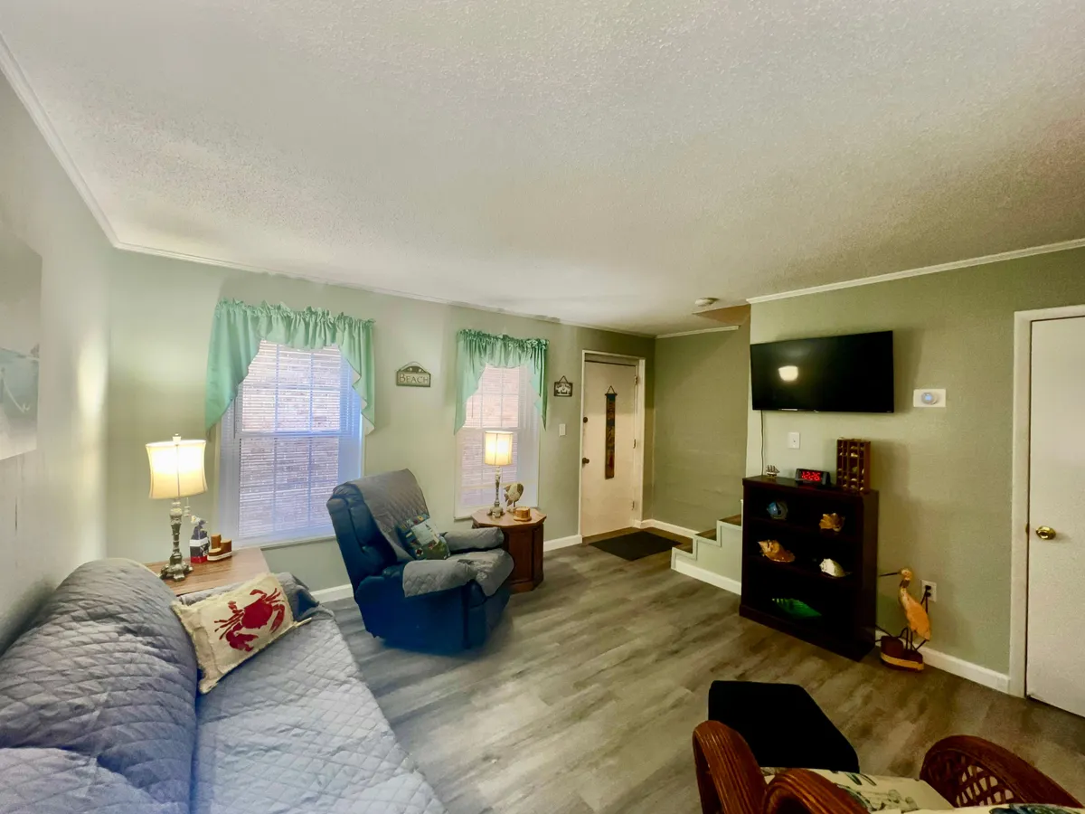 A bright living space with a comfortable sofa, floor lamp, TV for entertainment, and stairs leading to the upper level. The arrangement invites relaxation and shared experiences, with plenty of natural light enhancing the cheerful ambiance.