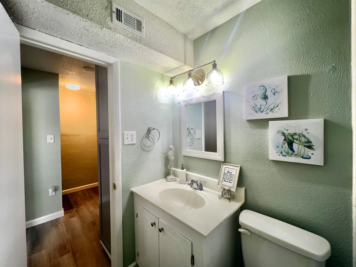 A bright and serene half bath, highlighted by a stylish sink, large mirror, gentle lighting, and wall artwork. The space feels fresh and convenient for guests.