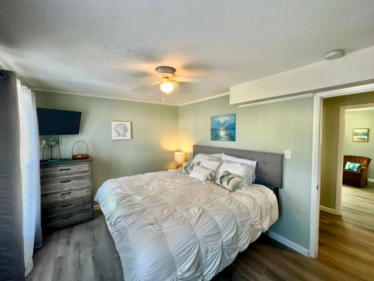 A restful bedroom featuring a king-sized bed adorned with decorative pillows and soft linens. There is a nightstand with a lamp for ambient lighting, and a dresser topped with a TV, creating a serene atmosphere ideal for relaxing after a busy day.