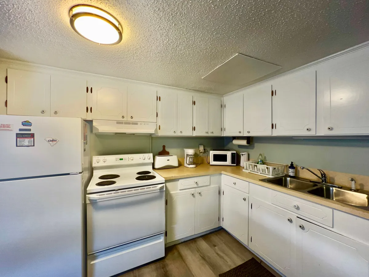 A close-up view of the kitchen workspace, featuring white cabinets, a stove, a sink, and generous countertop space. The setup is functional and inviting, signaling opportunities for meal prep and group cooking.