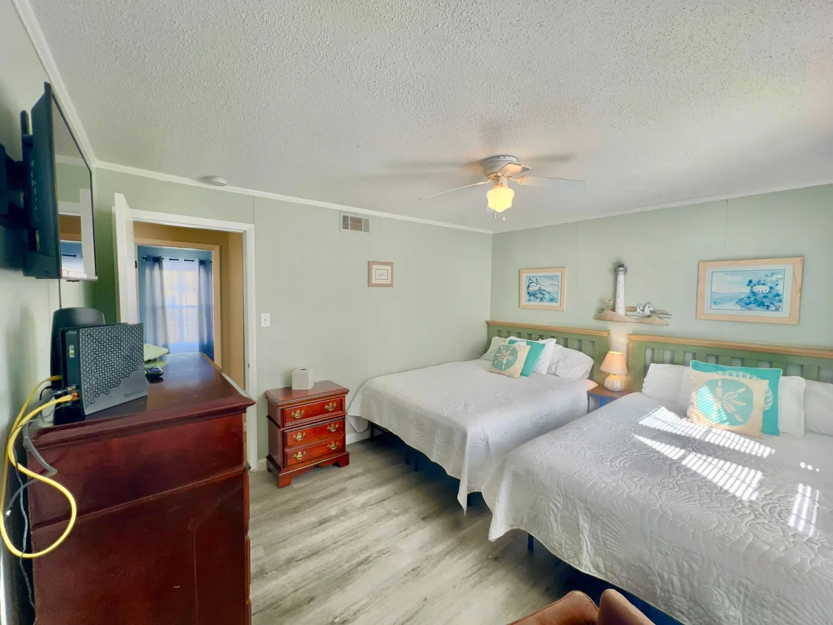A welcoming bedroom with two beds made up with decorative pillows, a dresser, and wall art. The space exudes comfort and is ideal for families or groups seeking a place to recharge together.