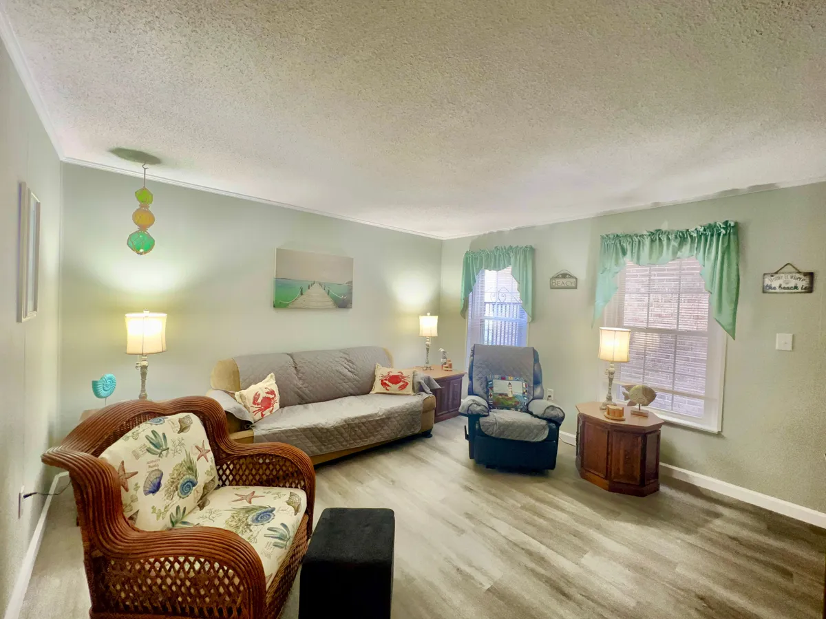A cozy living room featuring a plush sofa and armchair, a decorative lamp casting a warm glow, elegant curtains framing the window, and tasteful wall art adding personality. The layout suggests a welcoming space for relaxation, reading, or socializing.