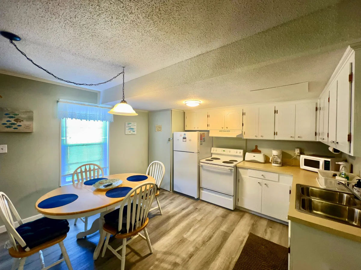 A bright, inviting dining table with blue placemats set for a meal, surrounded by white cabinetry and modern kitchen appliances. The space feels welcoming and functional, perfect for casual breakfasts or group gatherings.