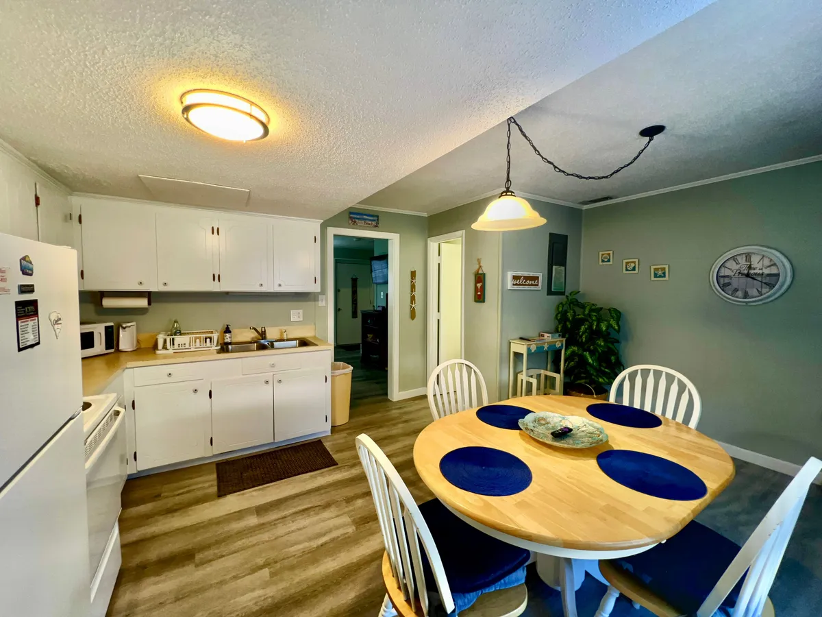 The image displays a kitchen table with blue placemats, complemented by white cabinetry and modern kitchen appliances in the background. The area appears ready for casual conversations, family gatherings, or dining celebrations.