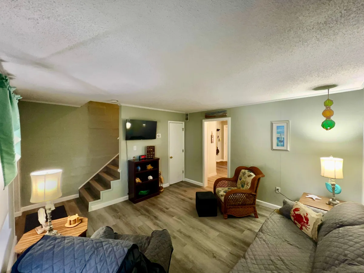The image displays a welcoming living area anchored by a cozy sofa, a stylish staircase, a decorative lamp, and artwork on the wall. The space is bright and open, ideal for unwinding together or planning a day’s adventure. The arrangement of furniture and soft lighting create an inviting atmosphere for couples to relax after exploring the local area.