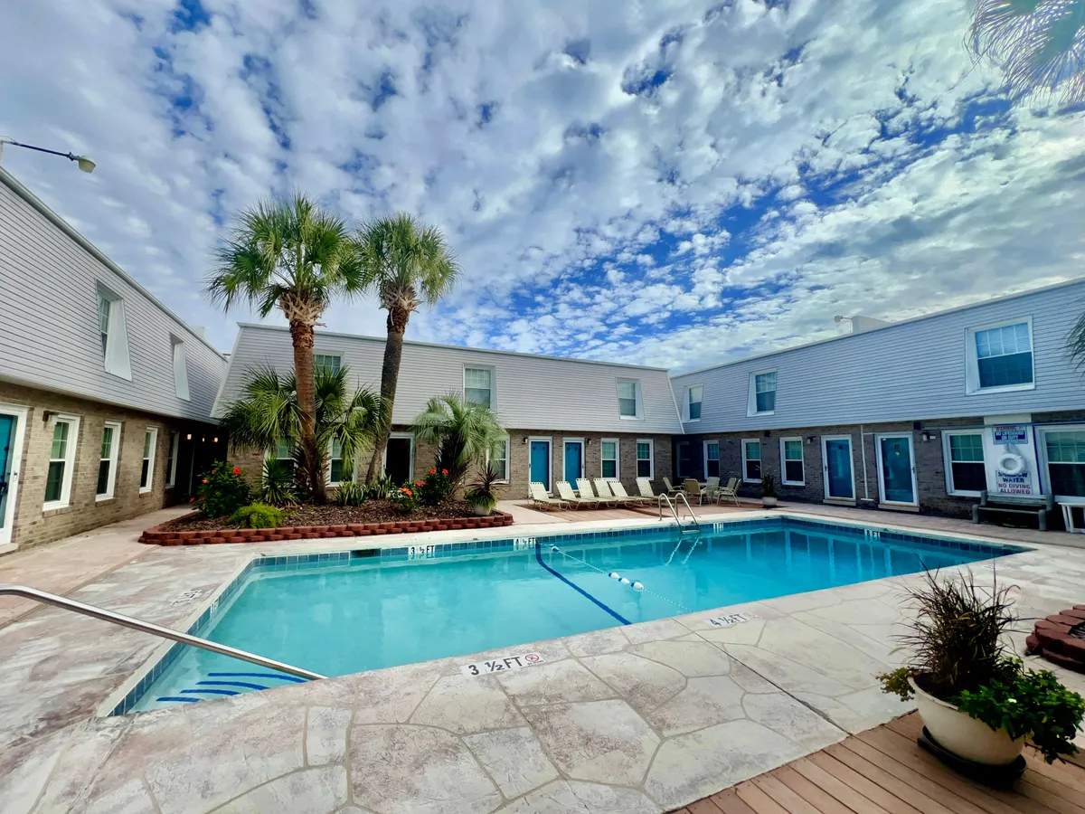 A vibrant outdoor scene featuring the shared swimming pool surrounded by palm trees, comfortable lounge chairs, and the backdrop of Madison Villa’s buildings. The space is filled with sunlight, inviting residents and guests to swim, sunbathe, or socialize by the water.